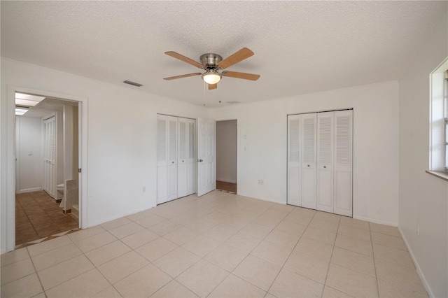 unfurnished bedroom with a textured ceiling, connected bathroom, two closets, and ceiling fan