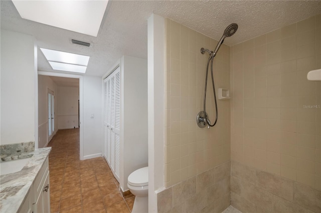 bathroom with a textured ceiling, vanity, a tile shower, and toilet