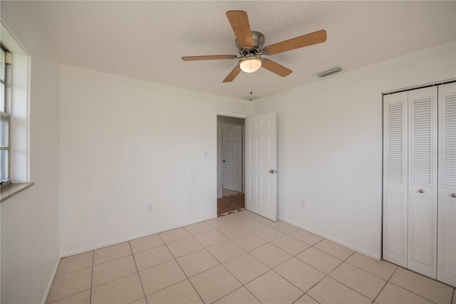 unfurnished bedroom with ceiling fan, light tile patterned flooring, a textured ceiling, and a closet