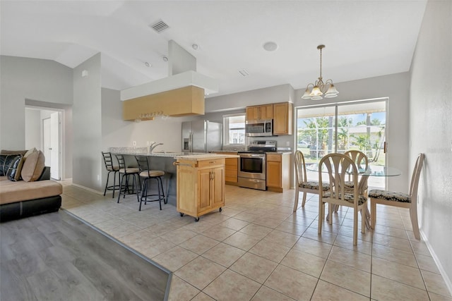 kitchen featuring appliances with stainless steel finishes, pendant lighting, a kitchen bar, vaulted ceiling, and a chandelier