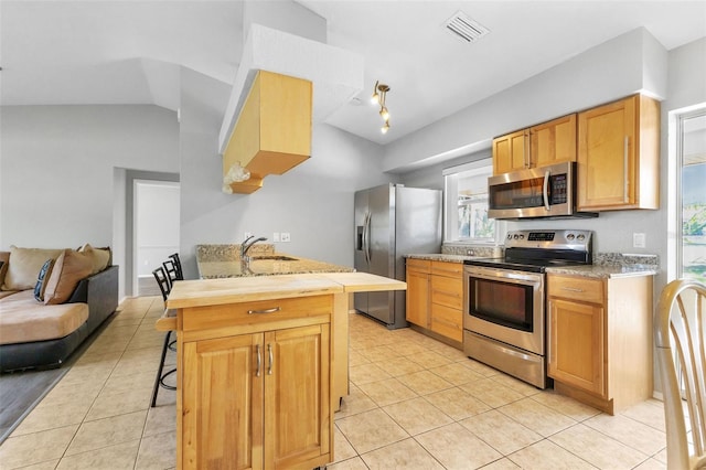 kitchen with a kitchen bar, stainless steel appliances, and light tile floors