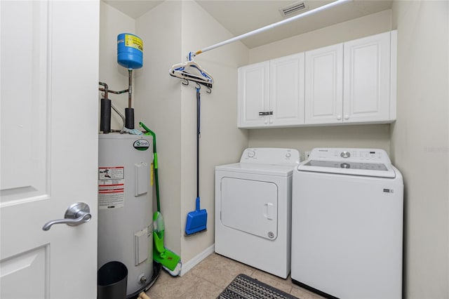 washroom featuring washing machine and dryer, water heater, light tile patterned floors, and cabinets