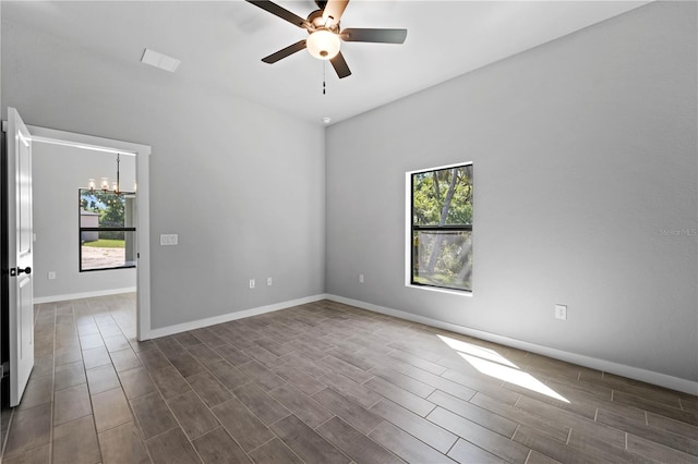 empty room featuring dark wood-type flooring, ceiling fan with notable chandelier, and plenty of natural light