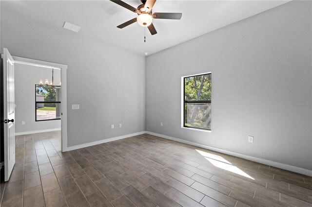 unfurnished room featuring ceiling fan with notable chandelier, plenty of natural light, and dark wood-type flooring