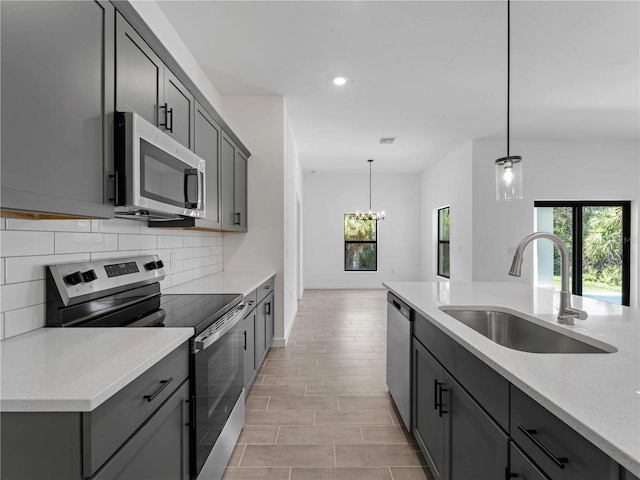 kitchen featuring light stone counters, sink, gray cabinetry, pendant lighting, and appliances with stainless steel finishes