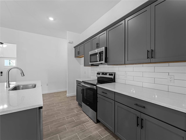 kitchen featuring light stone counters, appliances with stainless steel finishes, dark hardwood / wood-style flooring, gray cabinets, and sink