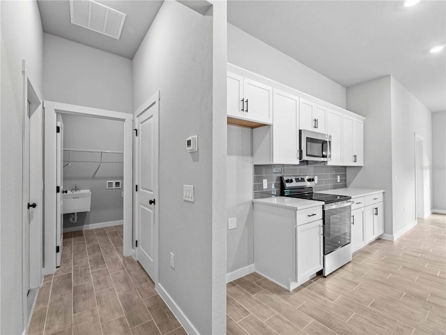 kitchen with white cabinets, light wood-type flooring, appliances with stainless steel finishes, and backsplash