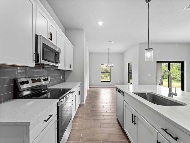 kitchen with light stone counters, stainless steel appliances, white cabinetry, decorative light fixtures, and sink