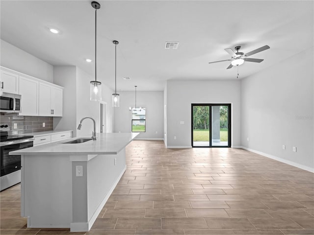 kitchen featuring a center island with sink, white cabinetry, sink, appliances with stainless steel finishes, and decorative light fixtures