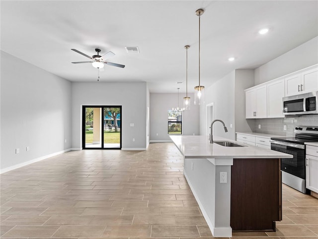 kitchen with stainless steel appliances, a center island with sink, white cabinets, sink, and decorative light fixtures