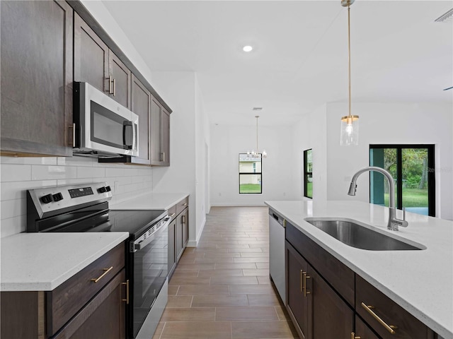 kitchen featuring light stone counters, appliances with stainless steel finishes, decorative light fixtures, dark brown cabinetry, and sink