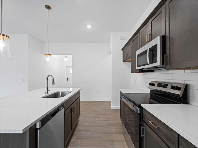 kitchen with light wood-type flooring, appliances with stainless steel finishes, light stone countertops, hanging light fixtures, and sink