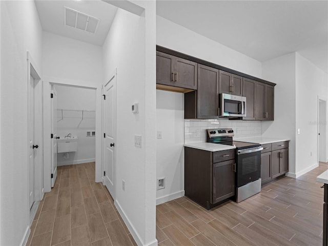 kitchen with tasteful backsplash, light wood-type flooring, appliances with stainless steel finishes, and dark brown cabinetry