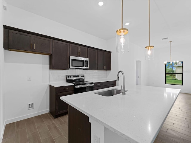 kitchen with stainless steel appliances, a kitchen island with sink, sink, and decorative light fixtures