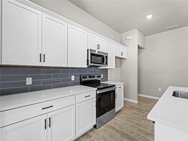 kitchen with stainless steel appliances, light hardwood / wood-style floors, white cabinetry, light stone countertops, and decorative backsplash