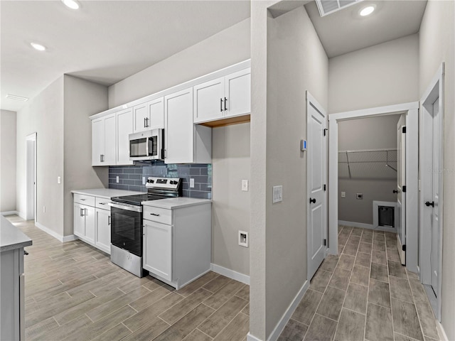 kitchen with white cabinets, decorative backsplash, appliances with stainless steel finishes, and light hardwood / wood-style flooring