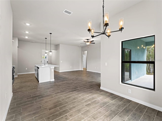 unfurnished living room featuring ceiling fan with notable chandelier, dark wood-type flooring, and sink