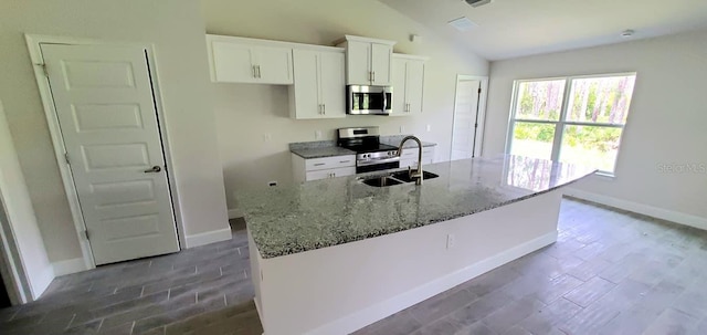 kitchen with white cabinets, a kitchen island with sink, stainless steel appliances, light stone countertops, and vaulted ceiling