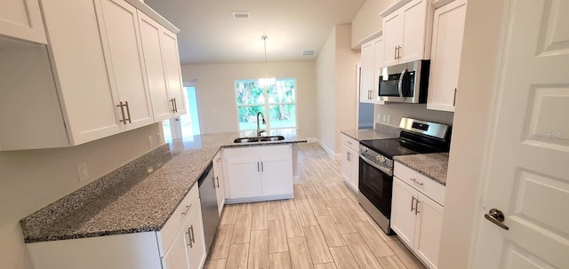 kitchen with stainless steel appliances, sink, pendant lighting, white cabinets, and dark stone countertops