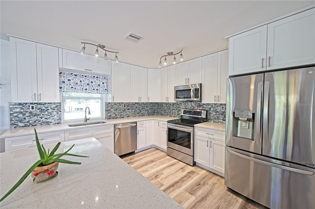 kitchen featuring stainless steel appliances, light hardwood / wood-style floors, sink, light stone countertops, and track lighting