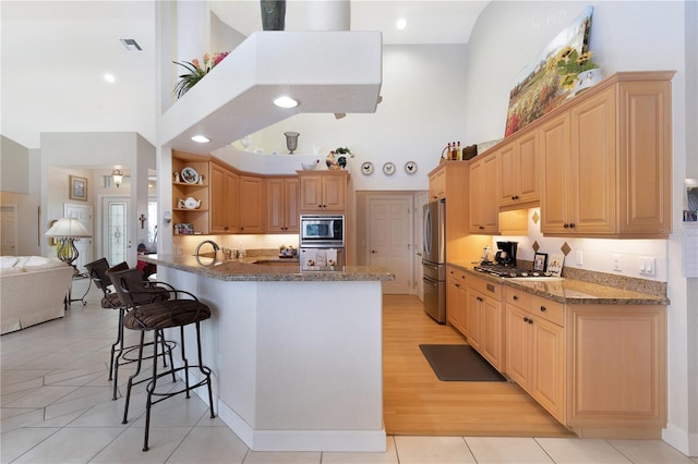 kitchen featuring appliances with stainless steel finishes, a kitchen bar, high vaulted ceiling, light tile floors, and dark stone countertops