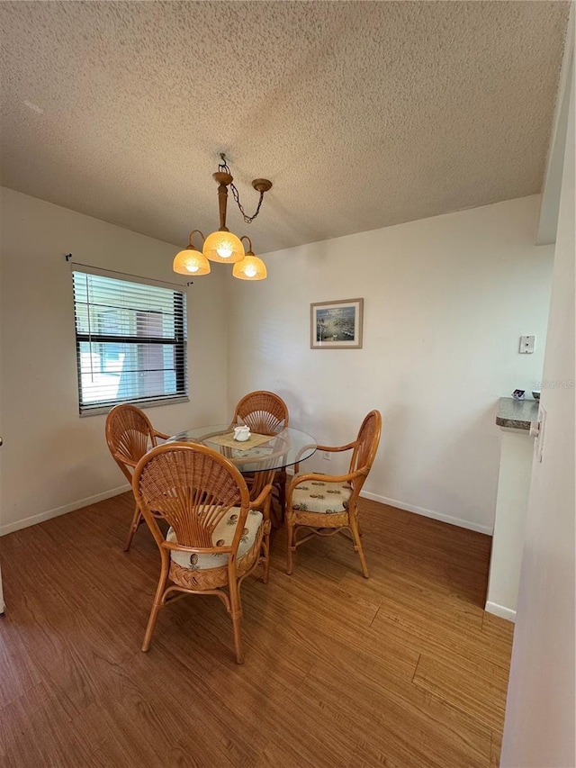 dining space featuring a textured ceiling, an inviting chandelier, wood finished floors, and baseboards