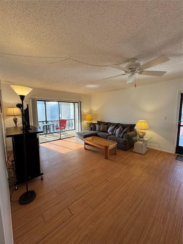 living room featuring ceiling fan, a textured ceiling, baseboards, and wood finished floors