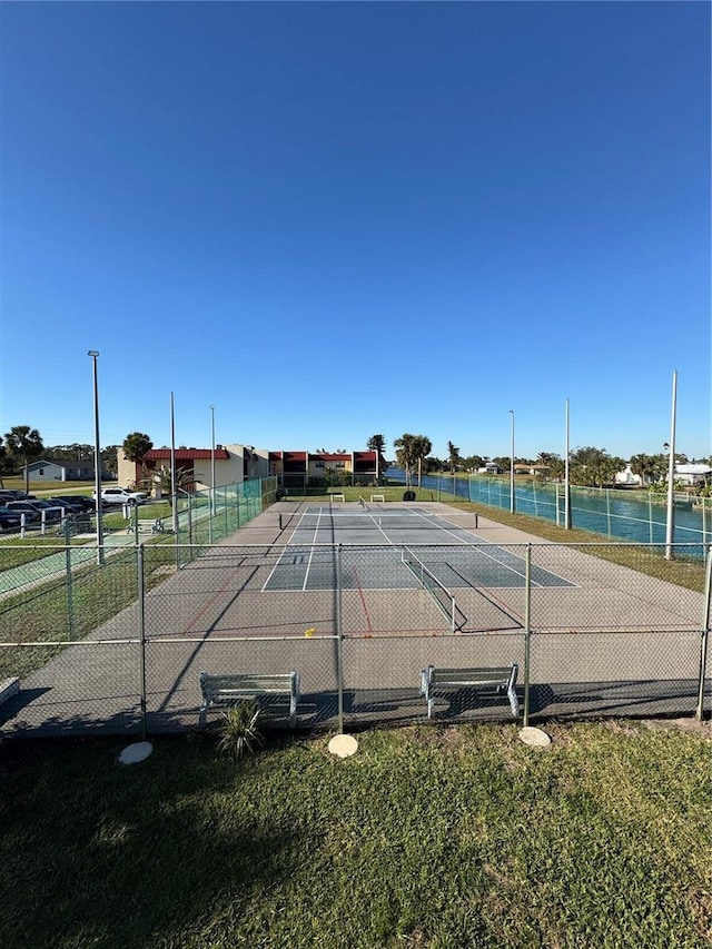 view of tennis court featuring a water view and fence