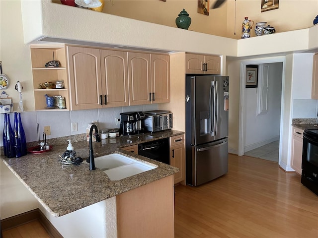 kitchen with dark stone countertops, black appliances, kitchen peninsula, sink, and light brown cabinetry