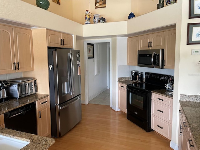 kitchen with a high ceiling, light wood-type flooring, light brown cabinetry, dark stone countertops, and black appliances