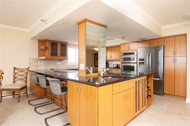 kitchen featuring appliances with stainless steel finishes, dark stone counters, sink, ornamental molding, and kitchen peninsula