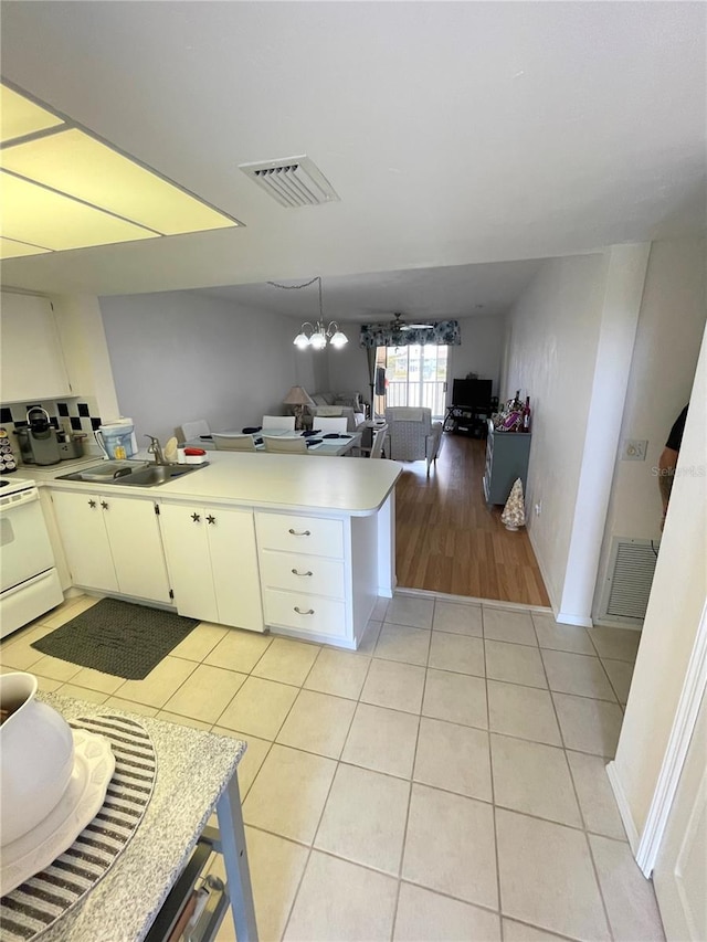 kitchen with light tile patterned floors, a chandelier, white electric range, sink, and kitchen peninsula