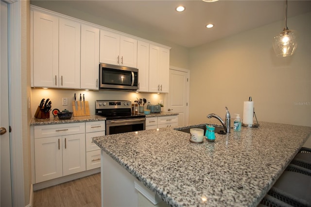 kitchen featuring light stone countertops, decorative light fixtures, appliances with stainless steel finishes, white cabinetry, and light wood-type flooring