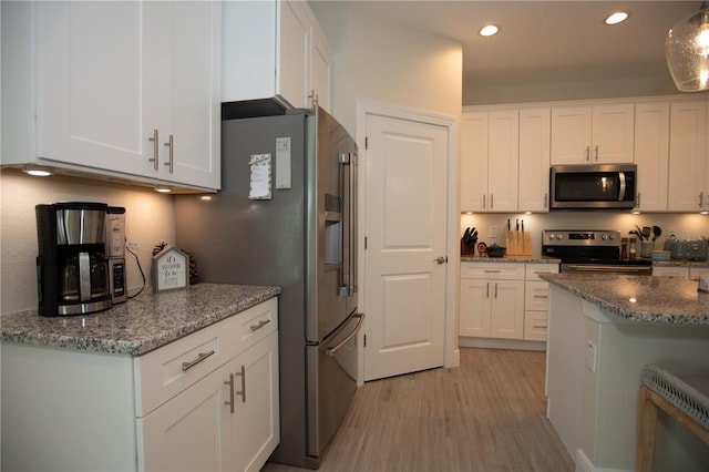 kitchen featuring stone counters, appliances with stainless steel finishes, hanging light fixtures, white cabinetry, and light wood-type flooring