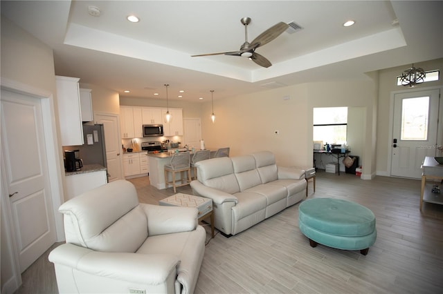 living room with a raised ceiling, ceiling fan, and light hardwood / wood-style floors