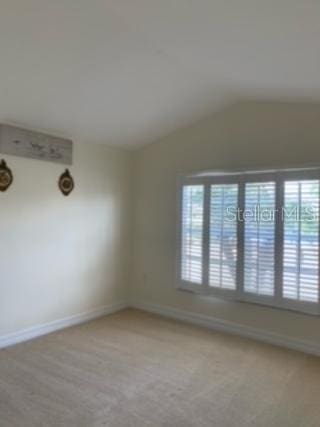 carpeted empty room featuring vaulted ceiling