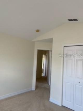 unfurnished bedroom featuring a closet, lofted ceiling, and light colored carpet