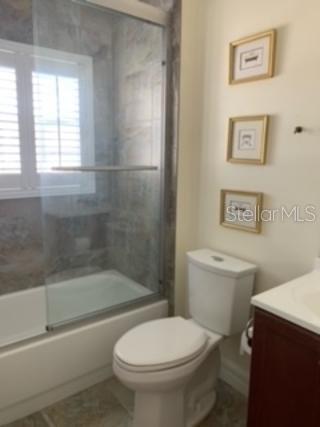 full bathroom featuring vanity, combined bath / shower with glass door, and toilet