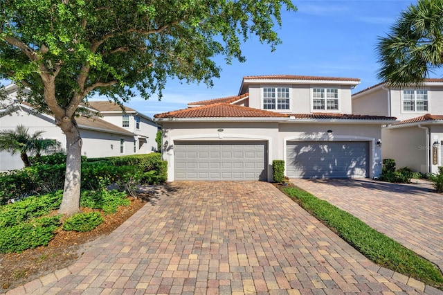 mediterranean / spanish-style house with decorative driveway, a tiled roof, an attached garage, and stucco siding