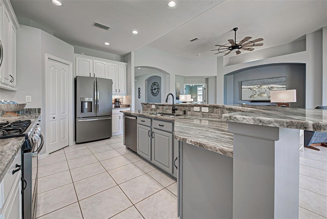 kitchen featuring appliances with stainless steel finishes, light tile floors, white cabinets, sink, and light stone countertops