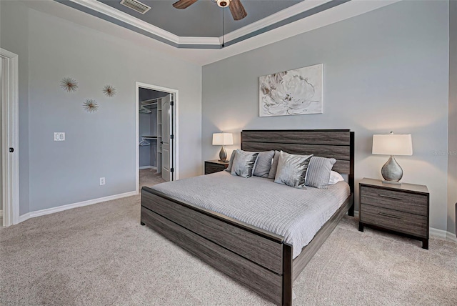 bedroom with a closet, ceiling fan, a tray ceiling, light colored carpet, and a walk in closet