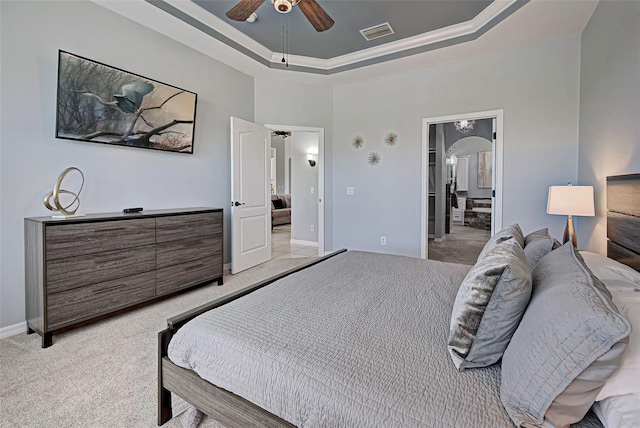 bedroom with ensuite bath, light colored carpet, ceiling fan, and a tray ceiling