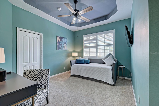 bedroom featuring light carpet, ceiling fan, a closet, and a raised ceiling