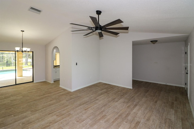 empty room with ceiling fan with notable chandelier, vaulted ceiling, and light wood-type flooring