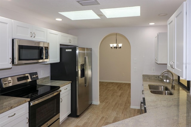 kitchen with white cabinetry, appliances with stainless steel finishes, sink, a skylight, and light hardwood / wood-style floors