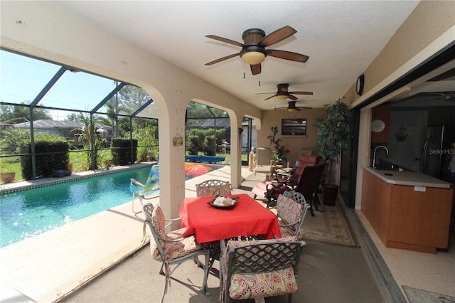 view of swimming pool featuring a patio area, sink, ceiling fan, and glass enclosure