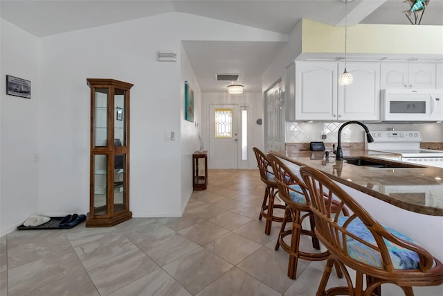 kitchen with white cabinets, white appliances, dark stone counters, hanging light fixtures, and vaulted ceiling