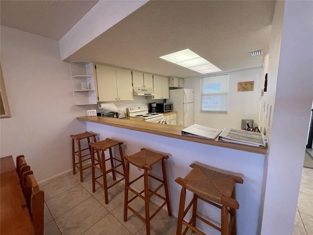 kitchen featuring a kitchen breakfast bar, kitchen peninsula, a textured ceiling, white appliances, and light tile patterned floors