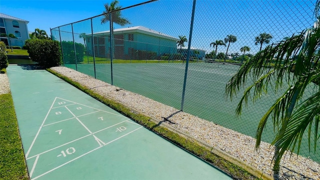 view of community featuring a tennis court, fence, and shuffleboard