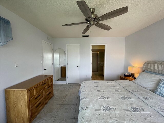 bedroom featuring ceiling fan, light tile patterned floors, and a textured ceiling